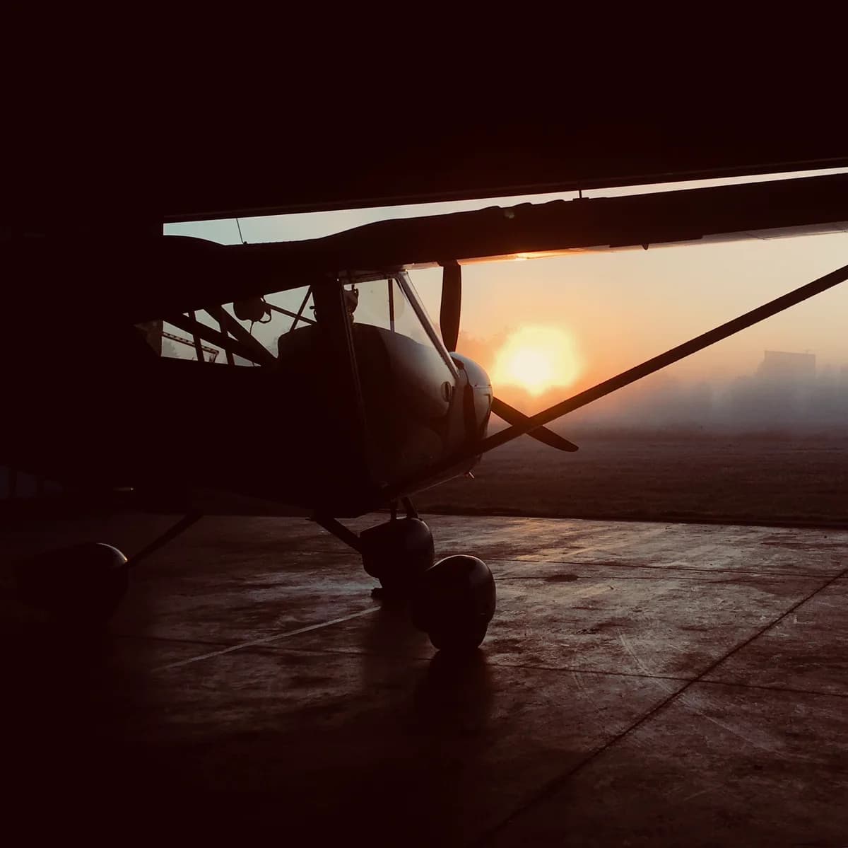 Silhouette of an Aeroprakt A-22LS at a hangar entrance in the evening sunlight