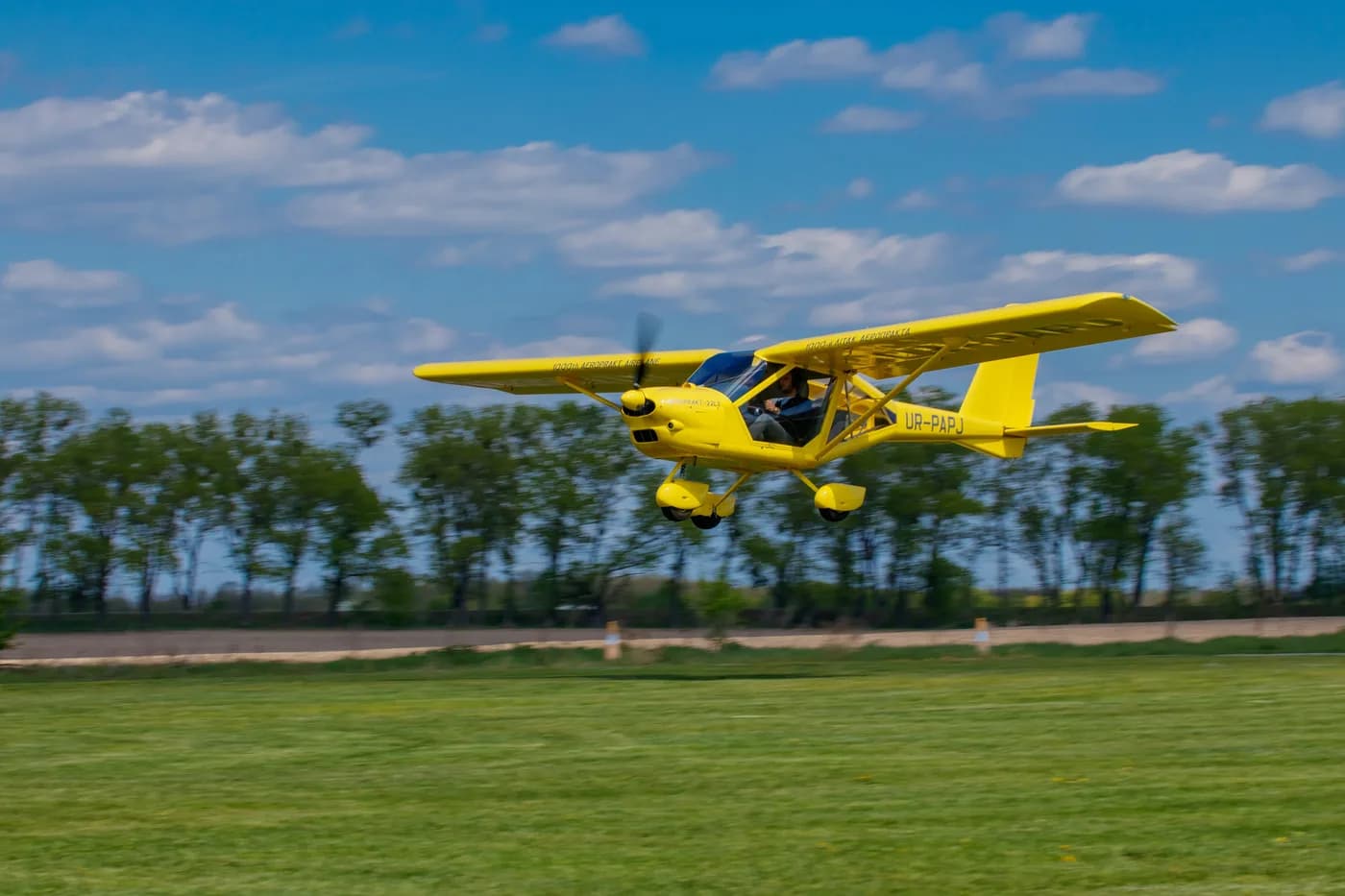 Yellow Aeroprakt A-22LS in flight just above a green airfield