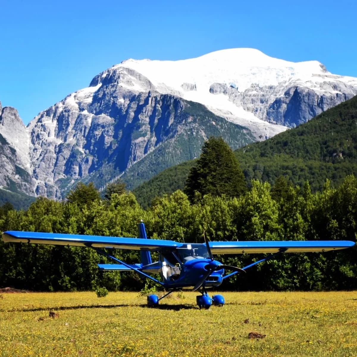 Blue Aeroprakt A-22LS parked on a grass airfield beneath snow-covered mountains
