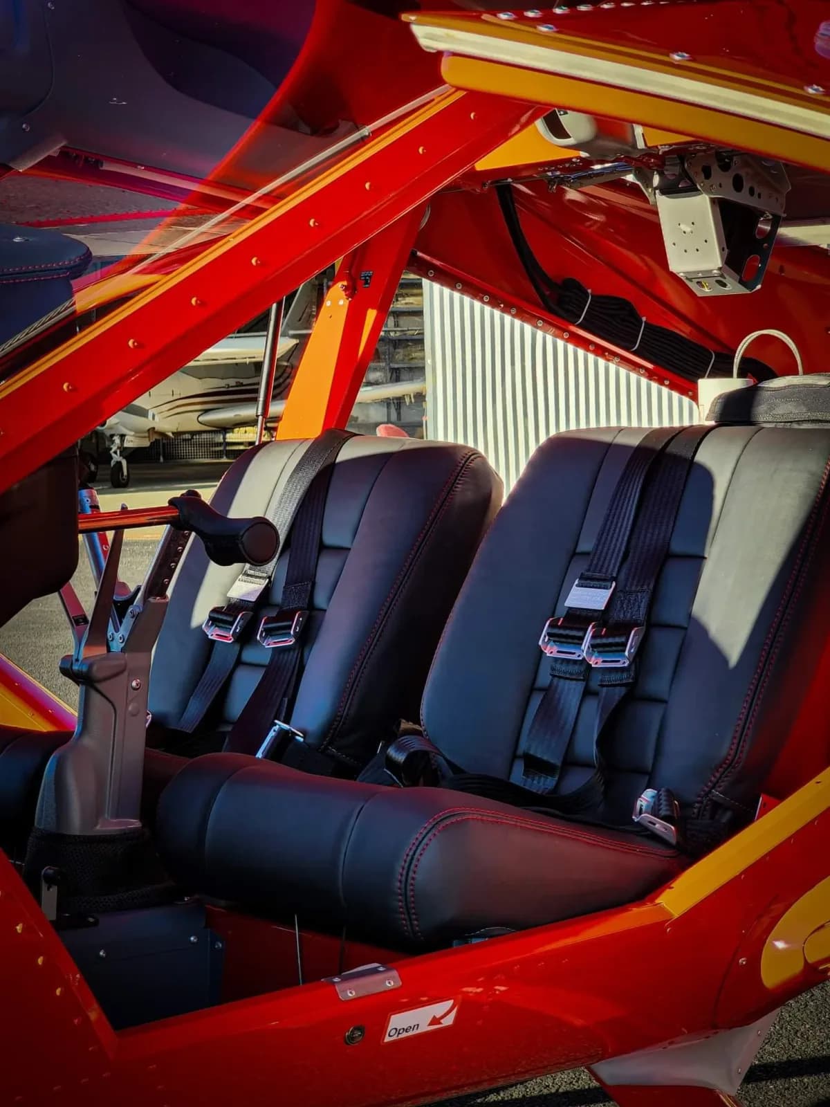 Side-by-side seats, harnesses and central Y-stick inside a red Aeroprakt A-32 cabin