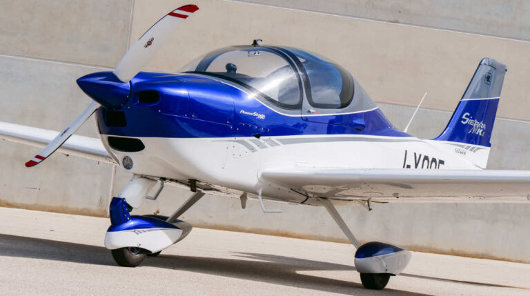 Blue and white P2002 Sierra MK II aircraft parked on the ground, featuring a sleek design with a bubble canopy and a single propeller.